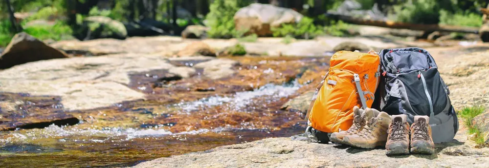 Two backpacks and some boots by a stream in nature